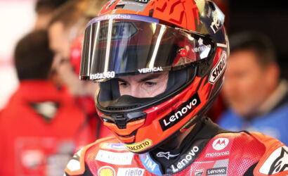 MotoGP rider wearing a red helmet with Lenovo and Motorola logos, close-up portrait in the pit area.