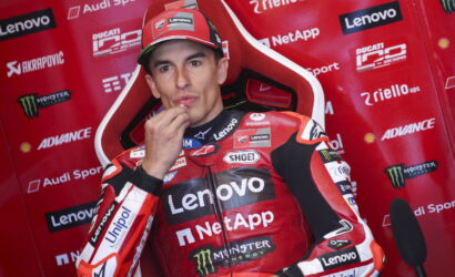 Motorcycle racer in red Lenovo-sponsored suit sits in a red sponsor wall, chin resting on hand, posing for interview.