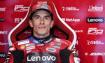 Portrait of a motorcycle racer in a red Lenovo-sponsored suit, seated against a red sponsor-filled backdrop.