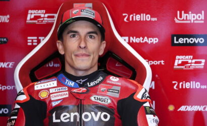Portrait of a motorcycle racer in a red Lenovo-sponsored suit, seated against a red sponsor-filled backdrop.