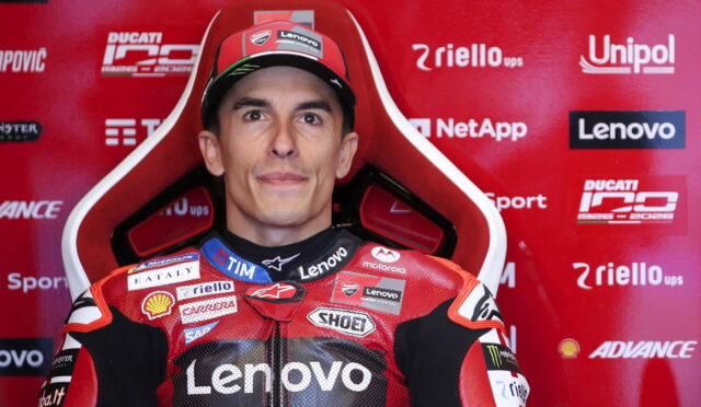 Portrait of a motorcycle racer in a red Lenovo-sponsored suit, seated against a red sponsor-filled backdrop.