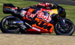 MotoGP rider in red bull KTM suit leaning into a high-speed left turn on a sponsor-laden race bike.