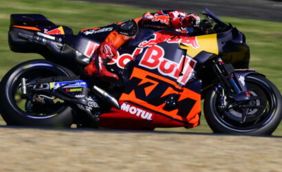 MotoGP rider in red bull KTM suit leaning into a high-speed left turn on a sponsor-laden race bike.