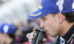 Man in a blue cap drinks from a Monster energy can at an outdoor event.