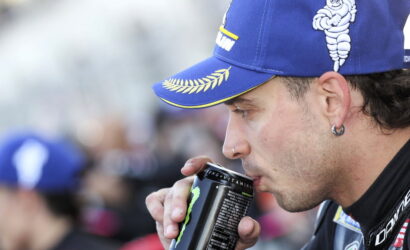 Man in a blue cap drinks from a Monster energy can at an outdoor event.