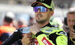 Motorsport rider in a neon yellow racing suit and mirrored sunglasses adjusting his collar before a race in the pit area