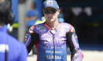 MotoGP rider in a purple Pramac Yamaha racing suit wearing sunglasses and a cap in the pit area.