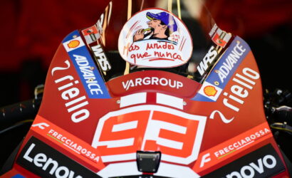 Close-up of a red racing motorcycle fairing covered in sponsor logos (Lenovo, Frecciarossa, Shell) with the number 93 and a circular sticker depicting a man smoking, against a dark background.