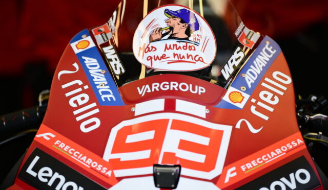 Close-up of a red racing motorcycle fairing covered in sponsor logos (Lenovo, Frecciarossa, Shell) with the number 93 and a circular sticker depicting a man smoking, against a dark background.