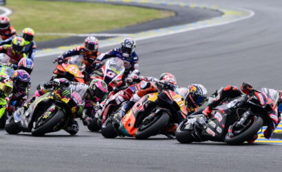 Motorcycle racers leaning into a sharp turn in a crowded group on a race track