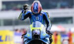 Motocross rider in a blue racing suit on a blue motorcycle raises a fist in celebration on the track