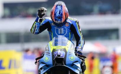 Motocross rider in a blue racing suit on a blue motorcycle raises a fist in celebration on the track