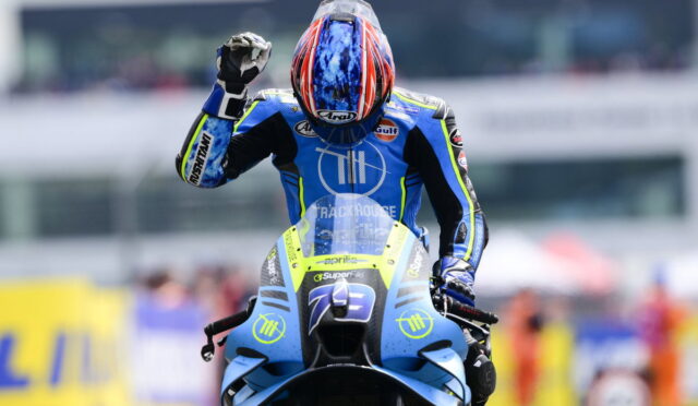 Motocross rider in a blue racing suit on a blue motorcycle raises a fist in celebration on the track