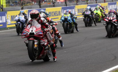 Motorcycle racers lean into a turn on a racing track, red Ducati leading the pack with Michelin barriers in the background