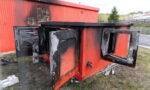 Red outdoor metal cabinet heavily burned, with doors open and charred interior panels visible.