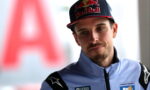 Portrait of a young man in a light-blue racing suit and a Red Bull cap, looking to the left.