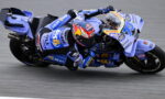 Motorcycle racer in blue racing suit leaning sharply into a turn on a race track in action.