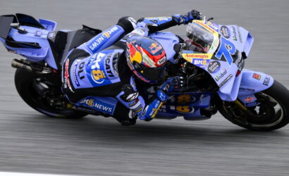 Motorcycle racer in blue racing suit leaning sharply into a turn on a race track in action.