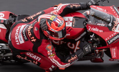 MotoGP rider in red Ducati leans into a turn on a red racing bike, wearing a matching helmet and suit.