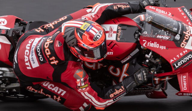 MotoGP rider in red Ducati leans into a turn on a red racing bike, wearing a matching helmet and suit.
