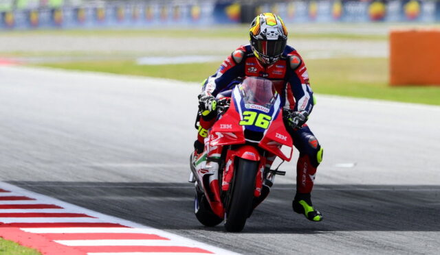 Moto racer in red-white-blue leathers leans into a left-hand turn on a track; bike number 36 visible on the red bike with sponsor logos.