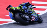 Motorcycle racer in neon yellow and blue gear leaning into a turn on a race track.