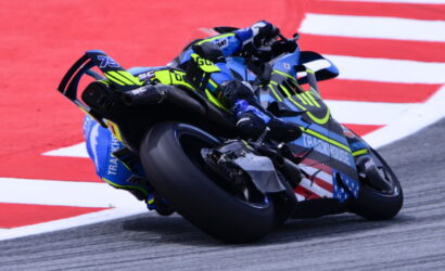 Motorcycle racer in neon yellow and blue gear leaning into a turn on a race track.