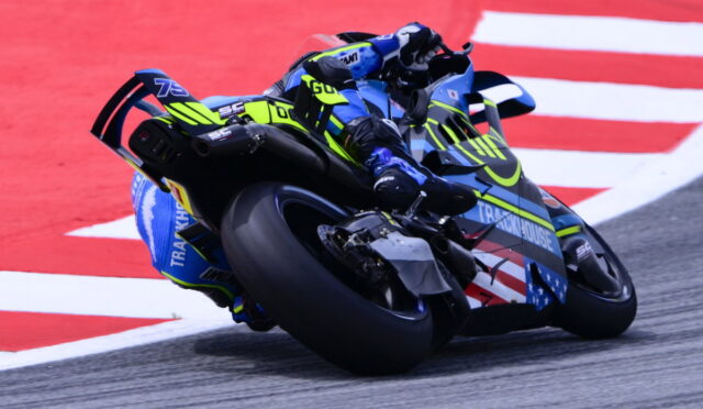Motorcycle racer in neon yellow and blue gear leaning into a turn on a race track.