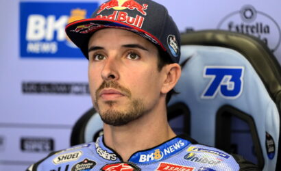 Portrait of a male motorcycle racer wearing a Red Bull cap, sitting in a blue race seat during an interview backdrop.