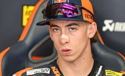 Portrait of a young motocross racer wearing a Red Bull cap and reflective goggles, with a bandage on his nose and a focused expression.