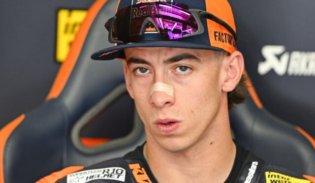Portrait of a young motocross racer wearing a Red Bull cap and reflective goggles, with a bandage on his nose and a focused expression.