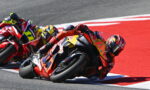 Motorcycle racers leaning into a sharp turn on a racetrack, with a red‑orange bike #93 in the foreground.