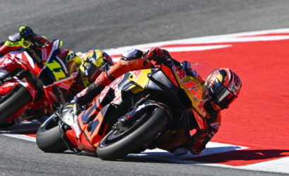 Motorcycle racers leaning into a sharp turn on a racetrack, with a red‑orange bike #93 in the foreground.