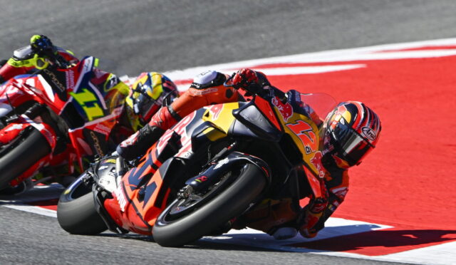 Motorcycle racers leaning into a sharp turn on a racetrack, with a red‑orange bike #93 in the foreground.