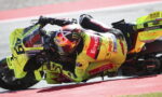 Motorcycle racer in a neon yellow suit and bike leaning into a sharp turn on a race track.