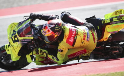 Motorcycle racer in a neon yellow suit and bike leaning into a sharp turn on a race track.