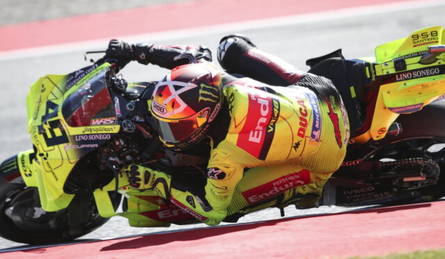 Motorcycle racer in a neon yellow suit and bike leaning into a sharp turn on a race track.