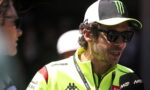 Man in a bright neon jacket being interviewed, wearing sunglasses and a black-and-white cap with a Monster logo, microphone nearby
