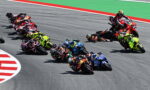 Group of motorcycle racers leaning into a sharp turn on a track, colorful racing bikes closely bunched together.
