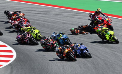 Group of motorcycle racers leaning into a sharp turn on a track, colorful racing bikes closely bunched together.