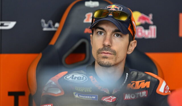 MotoGP rider in a KTM racing suit with Red Bull logos, seated in a chair against a branded backdrop.