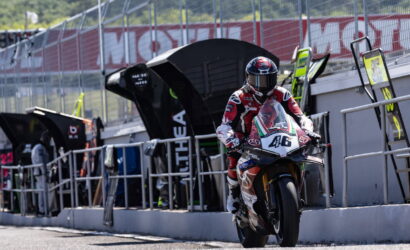 Rider in red and white racing gear on a sport motorcycle entering the pit lane, bike number 46 visible.