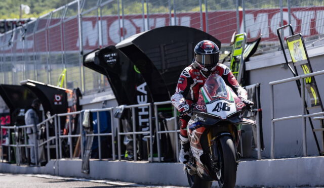 Rider in red and white racing gear on a sport motorcycle entering the pit lane, bike number 46 visible.