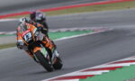 Motorcycle racer in orange and black suit leaning into a curve on a race track, bike numbered 73 with sponsor decals visible
