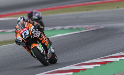 Motorcycle racer in orange and black suit leaning into a curve on a race track, bike numbered 73 with sponsor decals visible