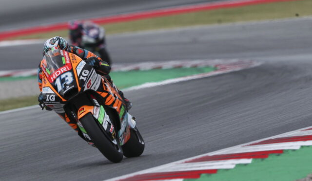 Motorcycle racer in orange and black suit leaning into a curve on a race track, bike numbered 73 with sponsor decals visible