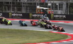 Group of motorcycle racers leaning into a sharp turn on a race track, Monster Energy banners in the background.