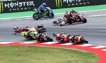 Motorcycle racers lean into a sharp turn on a race track with Monster Energy banners in the background.