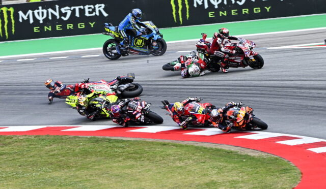 Motorcycle racers lean into a sharp turn on a race track with Monster Energy banners in the background.