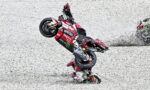 MotoGP rider crashes while performing a stunt on a red Ducati bike on a gravel track.